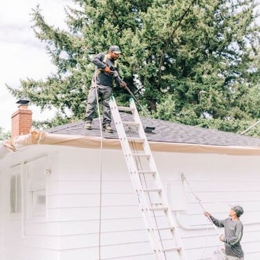 two service worker of rip city roof cleaning doing pressure washing the house